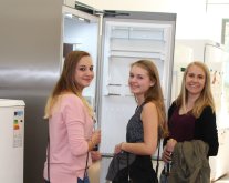 Drei junge Frauen stehen vor einem modernen Kühlschrank