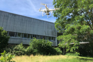 Weiße Minidrohne fliegt an modernem Gebäude entlang.