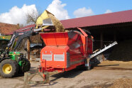 Grüner Traktor und rote Großmaschine stehen in einem Hof eines Landwirts.