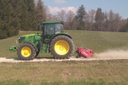 Traktor mit Anbaugerät zerkleinert Steine auf einem Forstweg.