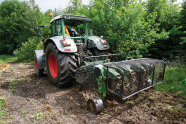 Ein grüner Traktor steht im Wald, hat hinten einen Anbau