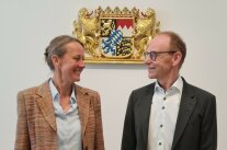 Portrait-Aunahme einer Frau und eines Mannes vor dem Bayerischen Staatswappen