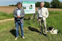 Zwei Männer stehen auf einer landwirtschaftlichen Wiese vor einer aufgestellten Infotafel