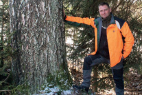 Mann vor dicker Moorbirke in warnorangener Jacke