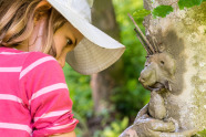 Mädchen bastelt mit Lehm ein Gesicht an einen Baum.