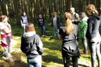 Eine Gruppe von Frauen stehen bei einer Waldführung um Kreis und hören dem Sprechenden zu.