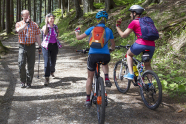 Zwei Mountainbiker begrüßen zwei Wanderer auf einem Waldweg.