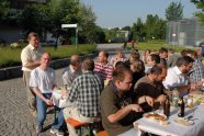 Einige Menschen sitzen auf Bierbänken an Biertischen im Freien und essen und trinken