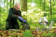 Ein Forscher, der neben einer Bodenstation eine Bodenprobe nimmt.