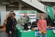 Ein Messestand in grün mit drei Besuchern und einem Mann hinter dem Stand