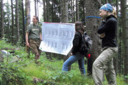 Drei Personen im Wald: zwei davon halten ein Poster zwischen sich