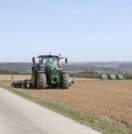 Eine Landmaschine fährt über einen Acker. Im Hintergrund sind Bienenvölker am Feldrand zu sehen.