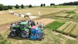 Traktor mit Anbaugerät, dahinter eine Gruppe von Menschen