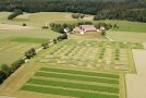 Luftbild auf landwirtschaftliche, kleinteilige Versuchsparzellen, im Hintergrund ein Wirtschaftsgebäude.