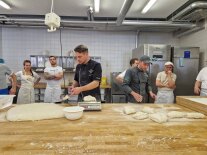 Mehrere Personen portionieren Teig auf einer Holzarbeitsbank in einer Lehrbackstube