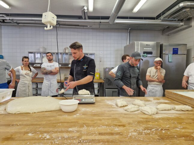 Mehrere Personen portionieren Teig auf einer Holzarbeitsbank in einer Lehrbackstube