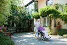 Seniorin im Rollstuhl wird von der Pflegefachkraft im Garten vom Schulhauser-Hof geschoben