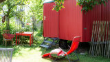 roter Liegestuhl vor rotem Holzcontainer-Anhänger in grüner Idylle