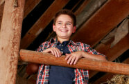 Ein Junge steht am Holzgeländer oben im Strohlager.