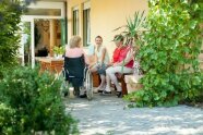 Pflegefachkräfte und Seniorinnen unterhalten sich auf der Terasse und lachen gemeinsam