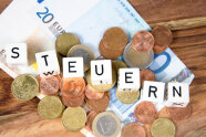 Euromünzen und Euroscheine mit Buchstabenwürfel, die den Text STEUERN ergebem.