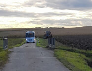 Bus auf einer kleinen Straße, daneben auf einem Acker steht ein Traktor