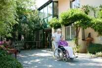 Seniorin im Rollstuhl wird von der Pflegefachkraft im Garten vom Schulhauser-Hof geschoben