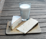Ein Glas Milch und zwei Stücke Käse auf einem Holzbrett