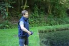 Ein junger Mann füttert in der Teichanlage des Instituts für Fischerei die Forellen mit Ölpresskuchenanteile