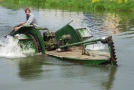 Mann in einem Wasserpflanzen-Mähboot auf dem Wasser