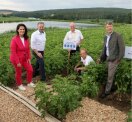 Fünf Personen stehen an einem Feld mit Bewässerungsanlage neben einem Teich.