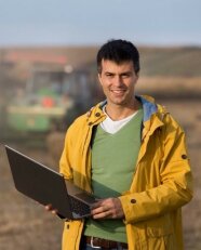 EIT-Foot-Mitarbeiter: Ein junger Mann mit steht mit dem aufgeschlagenen Laptop auf dem Arm auf einem Feld.