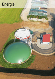 Eine Biogasanlage mit grün abgedecktem runden Nachgärbehälter und Futtersilos im Hintergrund aus der Luft fotografiert