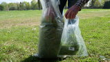 Ein Mann nimmt aus einem Sack Gras an verschiedenen Stellen heraus und steckt es in eine separate Tüte.