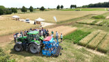 Personen vor einer Landmaschine auf einem Feld mit Versuchsparzellen.