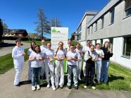 Dreizehn Personen stehen mit kleinen Eisbechern vor einem Gebäude