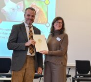 Dr. Jan Harms von der LfL nimmt den Zuwendungsbescheid für das Netzwerk Fokus Tierwohl in Bayern von der Staatssekretärin Dr. Ophelia Nick entgegen. Beide stehen auf einer Bühne.