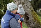 Ein Mann hebt ein Kind hoch, damit es in das große Astloch eines Baumes blicken kann.
