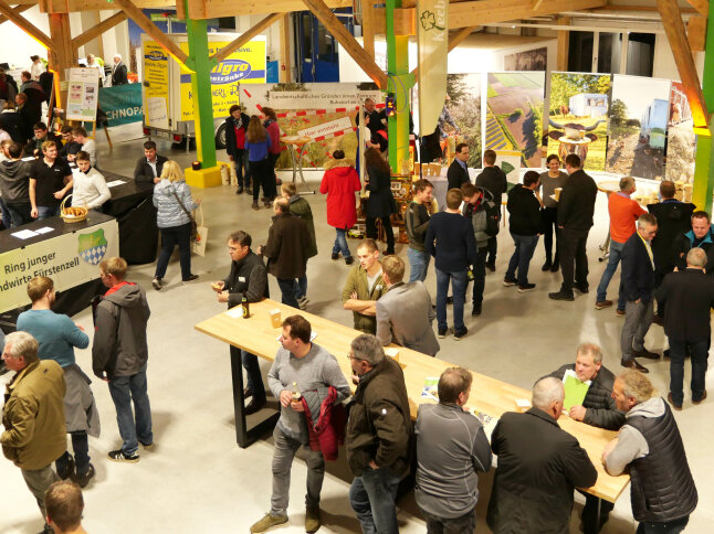 Mehr als 35 Menschen befinden sich auf einer Veranstaltung in einer Halle mit Infotafeln