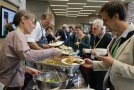 Vier Personen geben einer Reihe von anderen Personen Essen aus