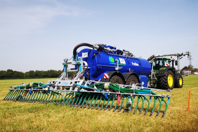 Ein Traktor mit Güllefass fährt auf einer Wiese mit Schleppschuhtechnik Gülle.